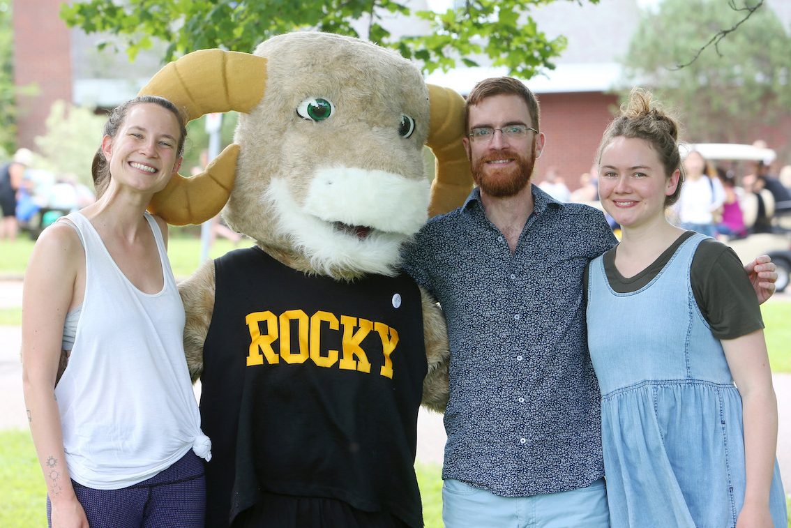 Ram mascot stands with arms around three people.