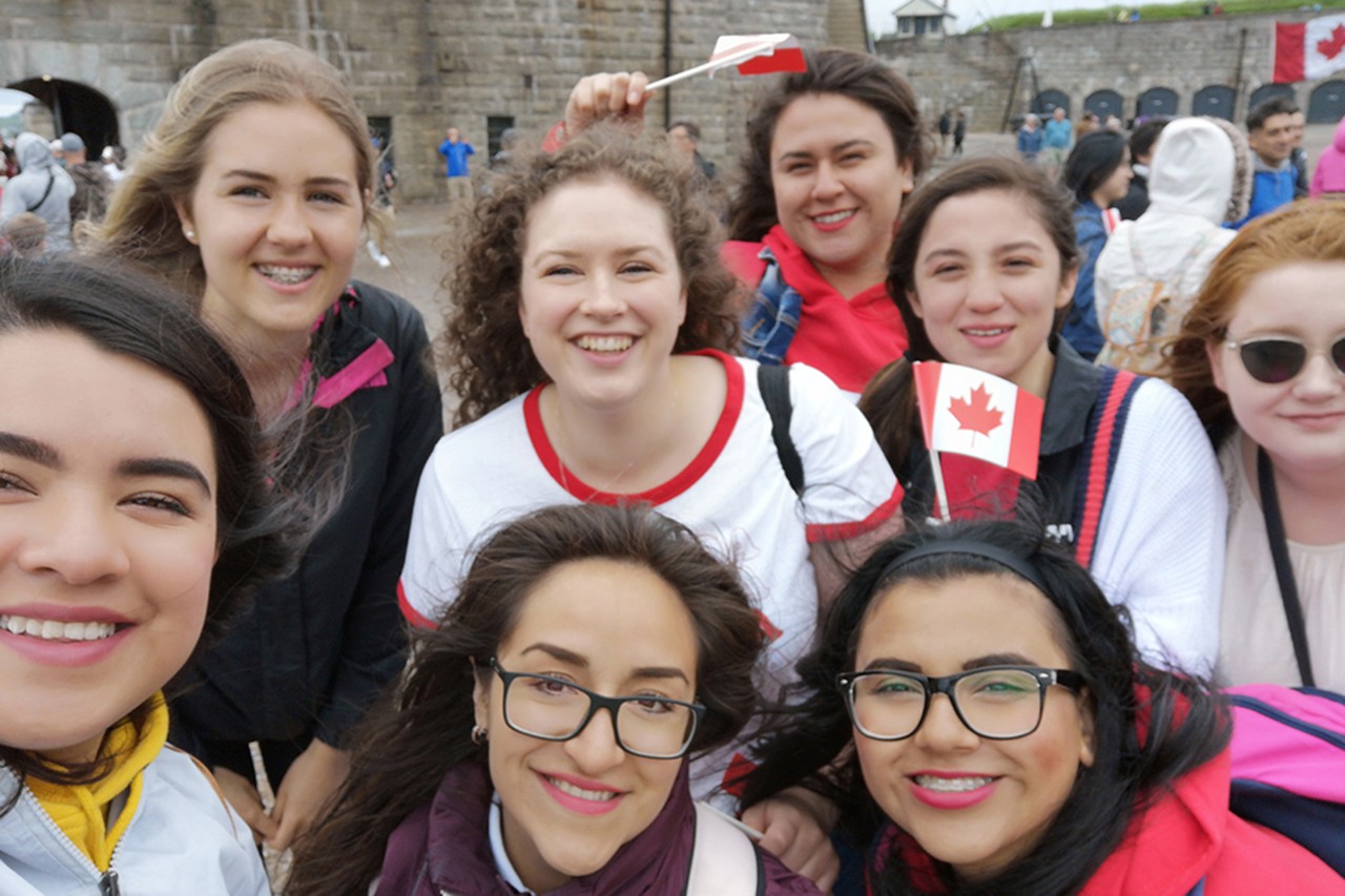 A small group of female students standing close to the camera waving Canada flags.