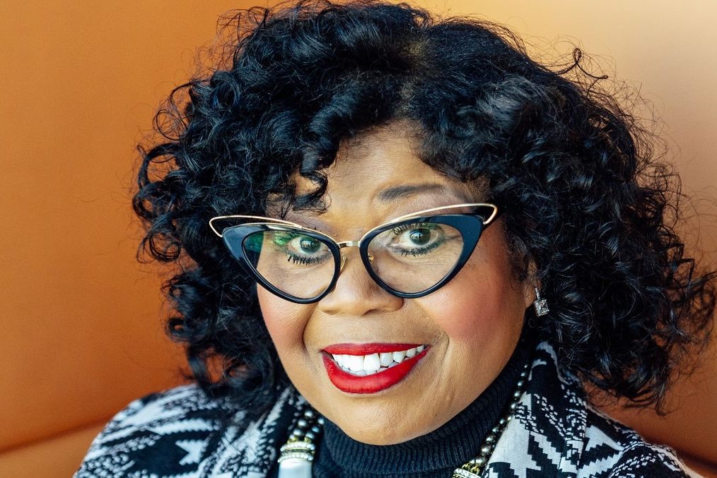 Smiling black woman wearing glasses and a statement necklace.