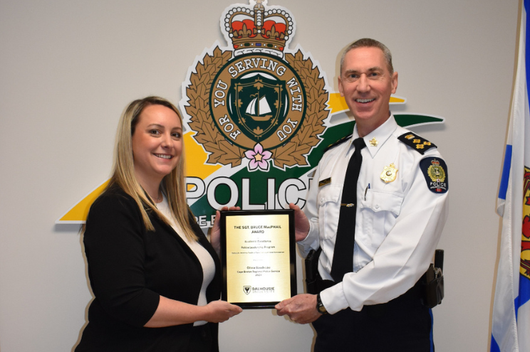 A female and a man in uniform are standing on either side of a plaque and holding it while smiling.