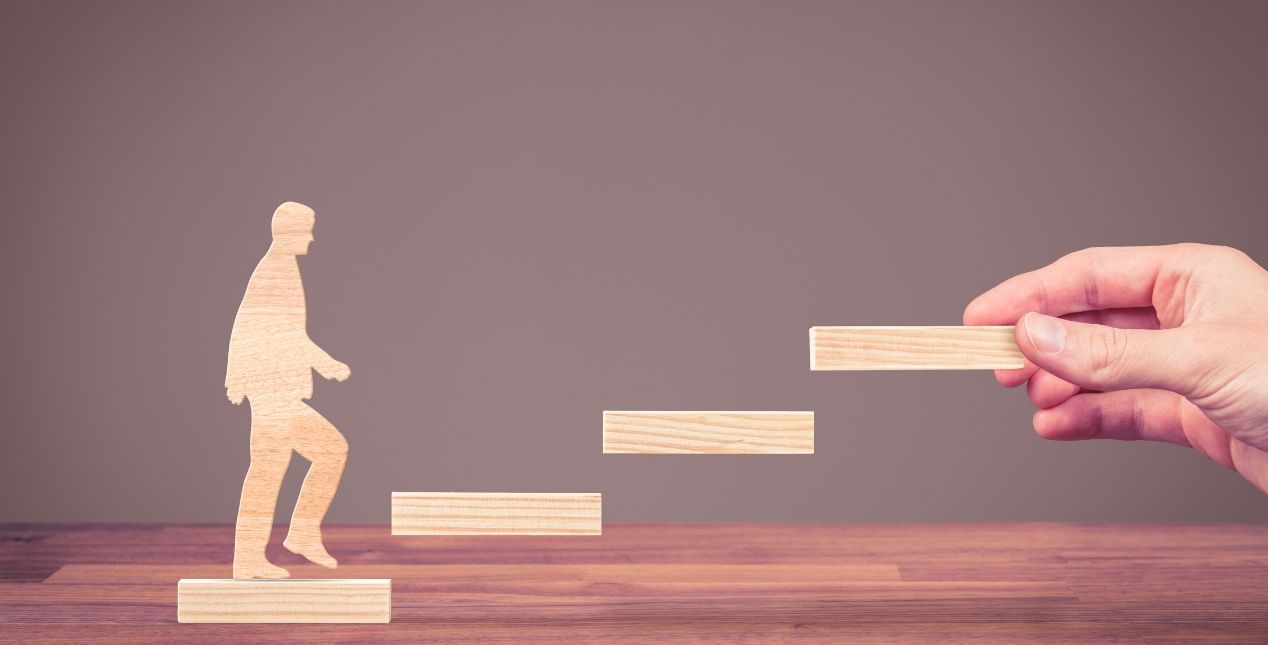 a hand holding up a step for a wooden man to climb up.