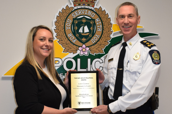 A female and a man in uniform are standing on either side of a plaque and holding it while smiling.