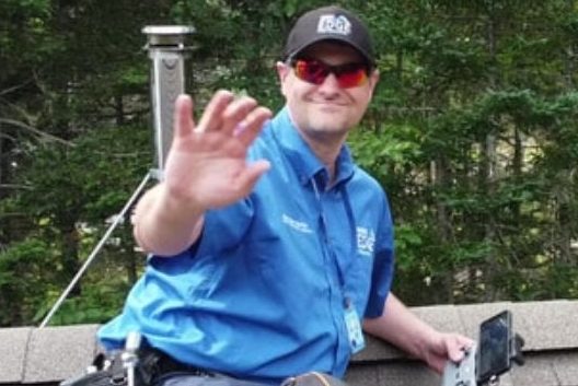 Man on roof with inspection gear waving to the camera