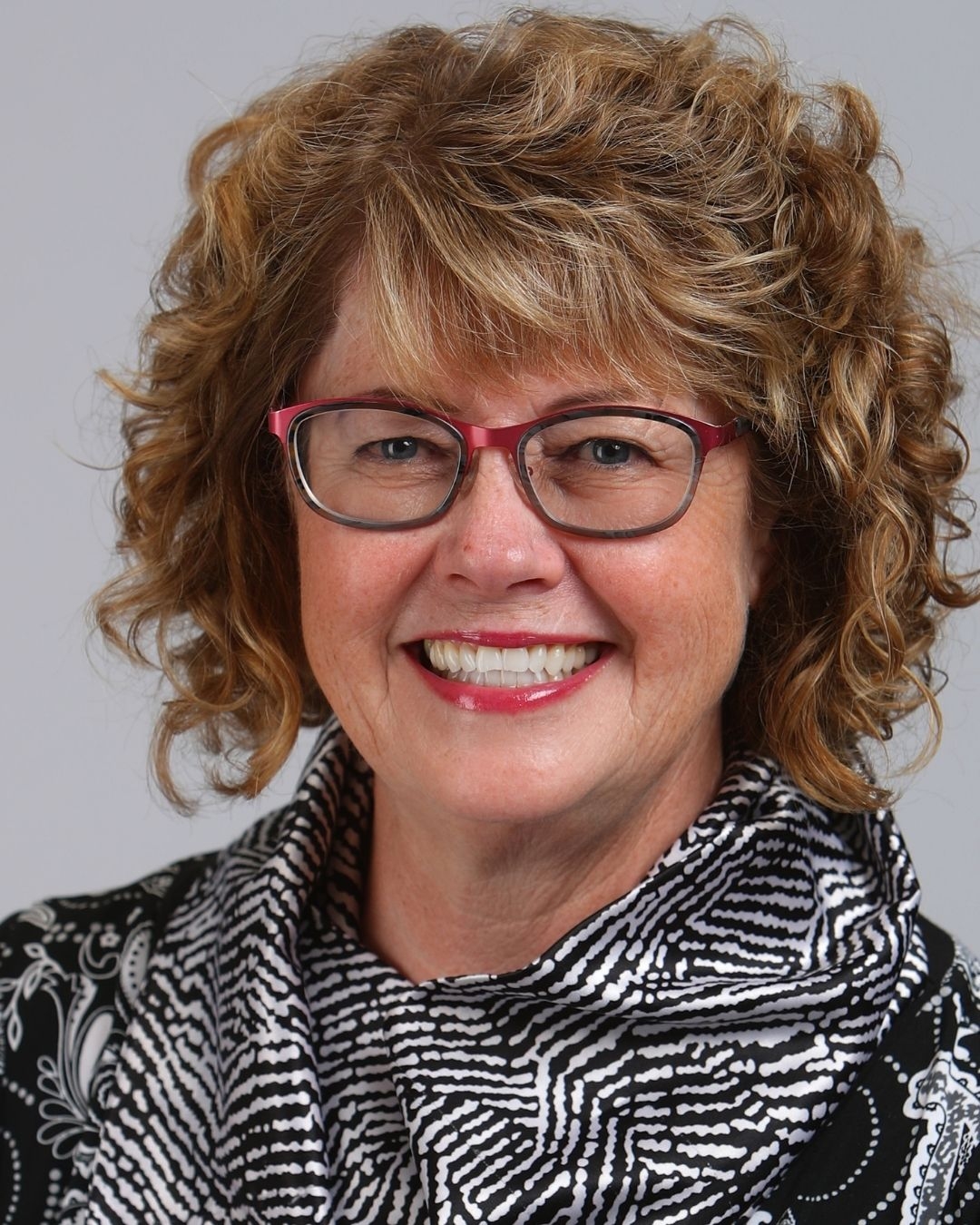 Woman with curly blonde hair wearing red glasses.