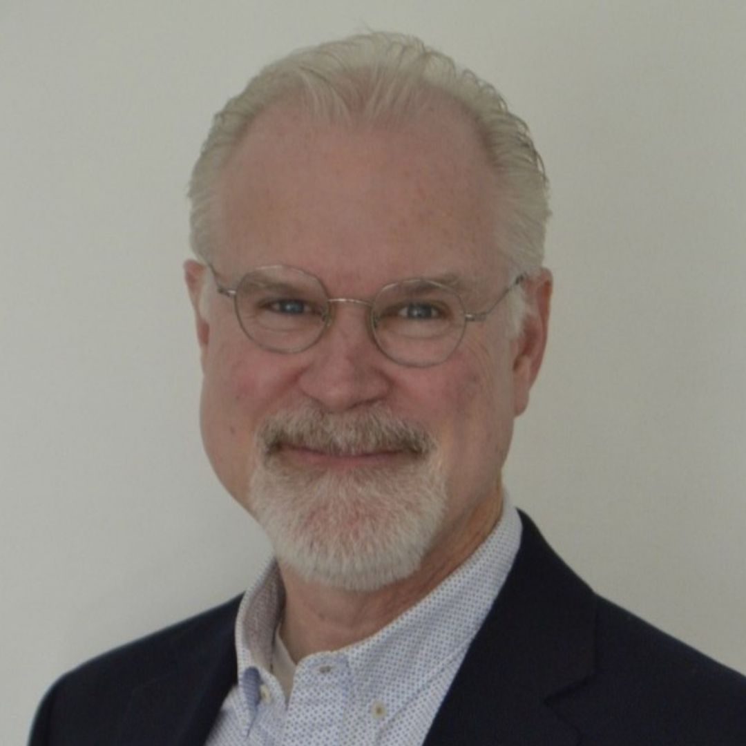 A man with white hair wearing round wire-framed glasses.