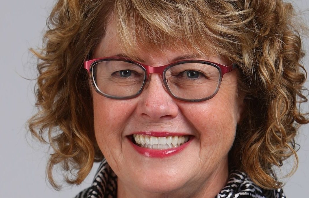 Woman with curly blonde hair wearing red glasses.