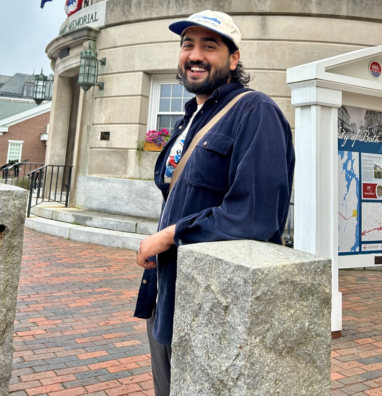 A man wearing a hat leaning on a concrete pillar.