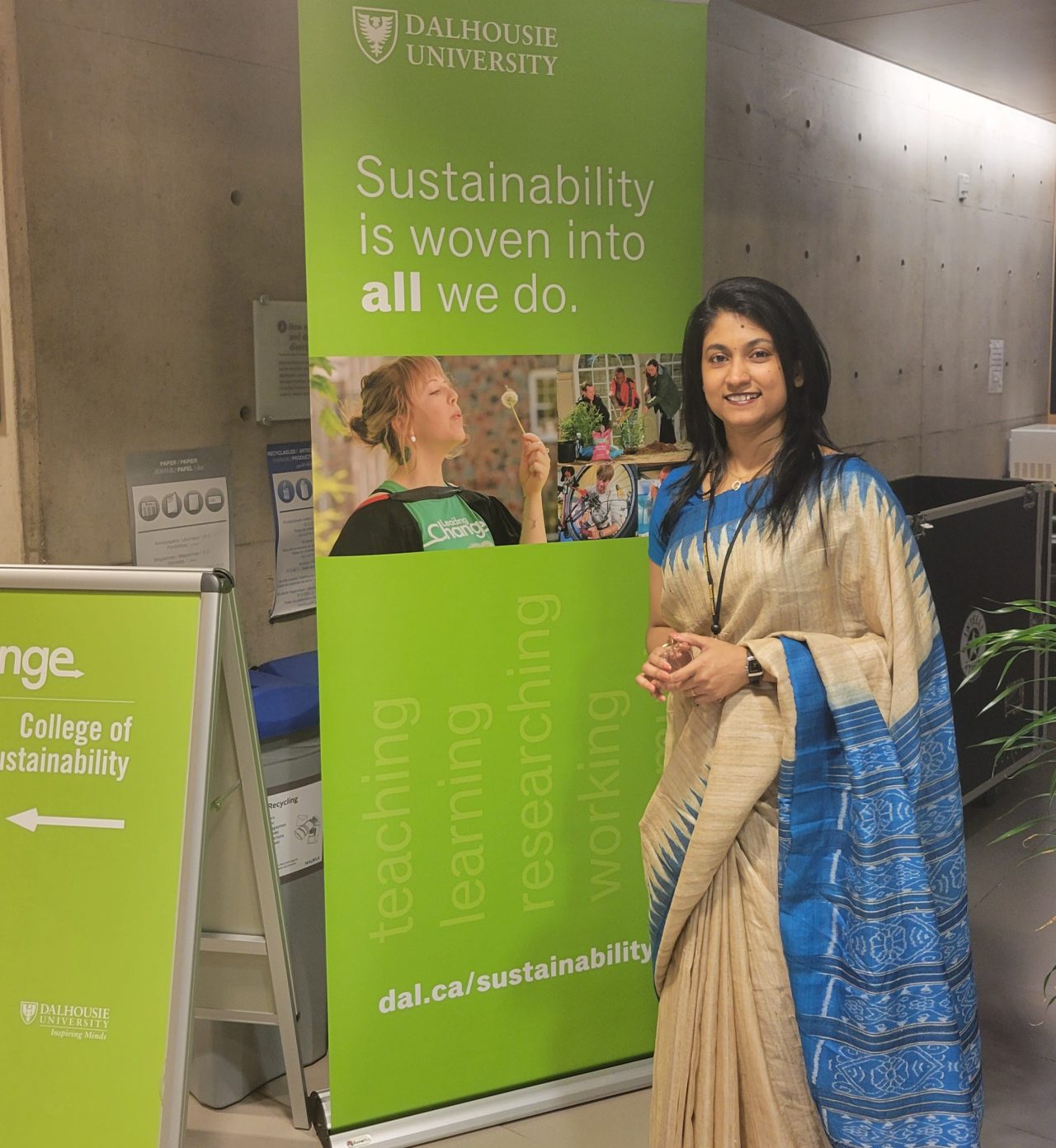 Woman in a sari stands by Dalhousie University's College of Sustainability banners, showcasing a modern, professional, and educational setting.