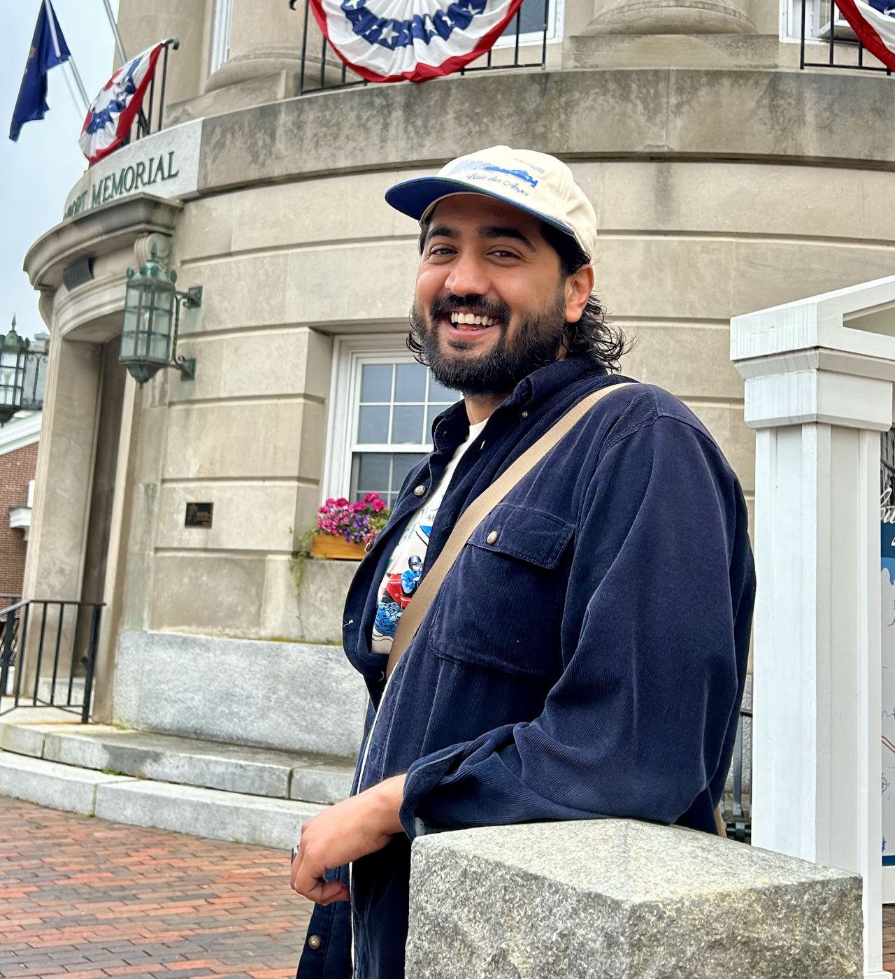 A man leaning on a concrete pillar wearing a hat. 