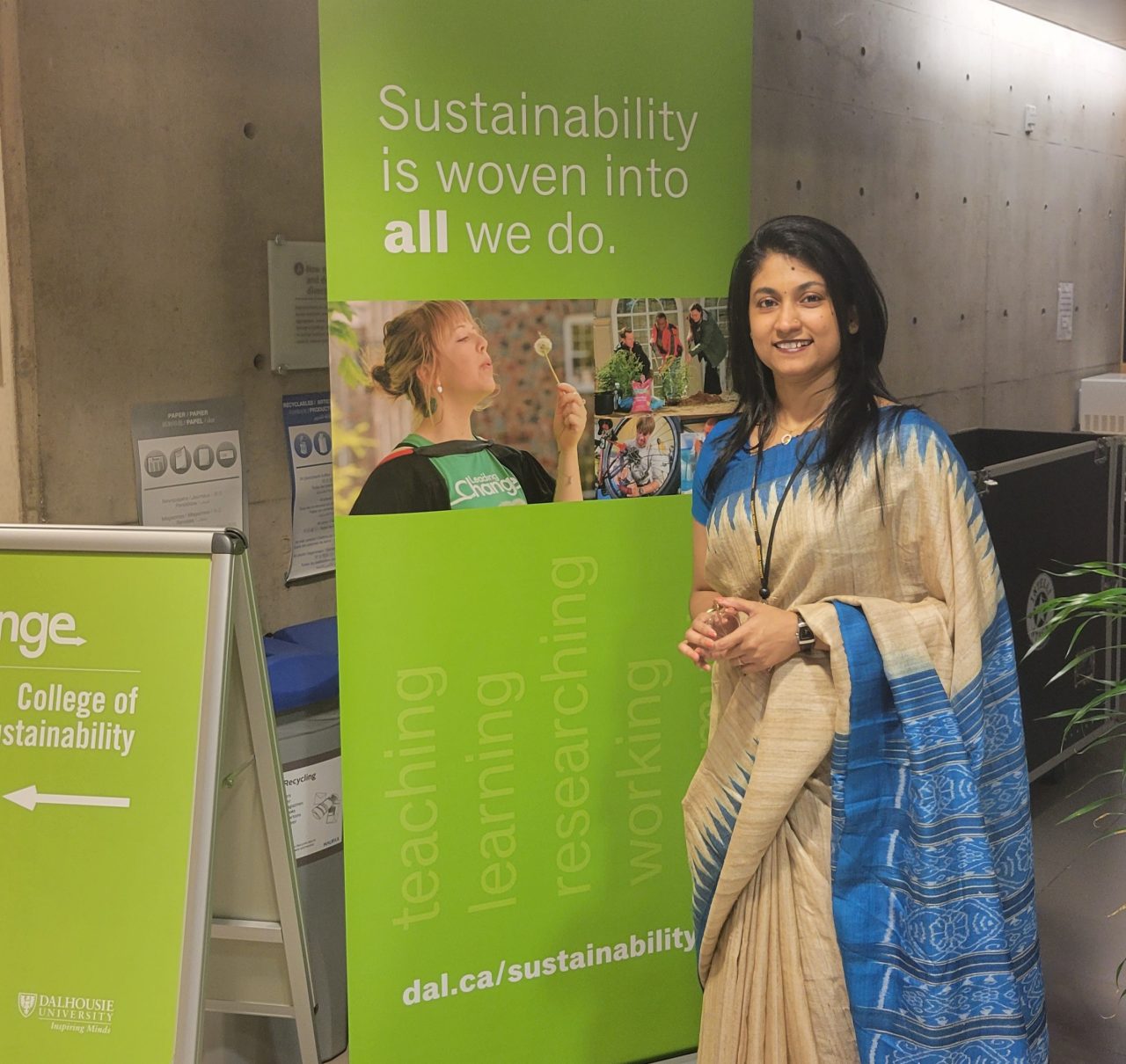 A female learner standing in front of a sign and smiling.