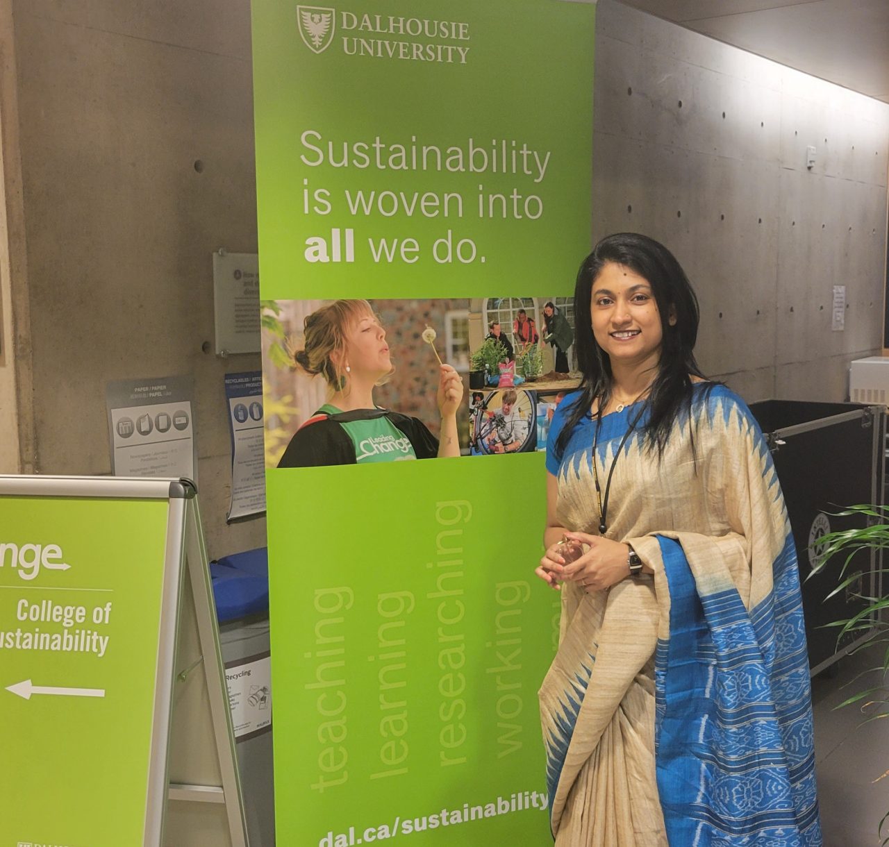 A female learner standing in front of a sign and smiling.