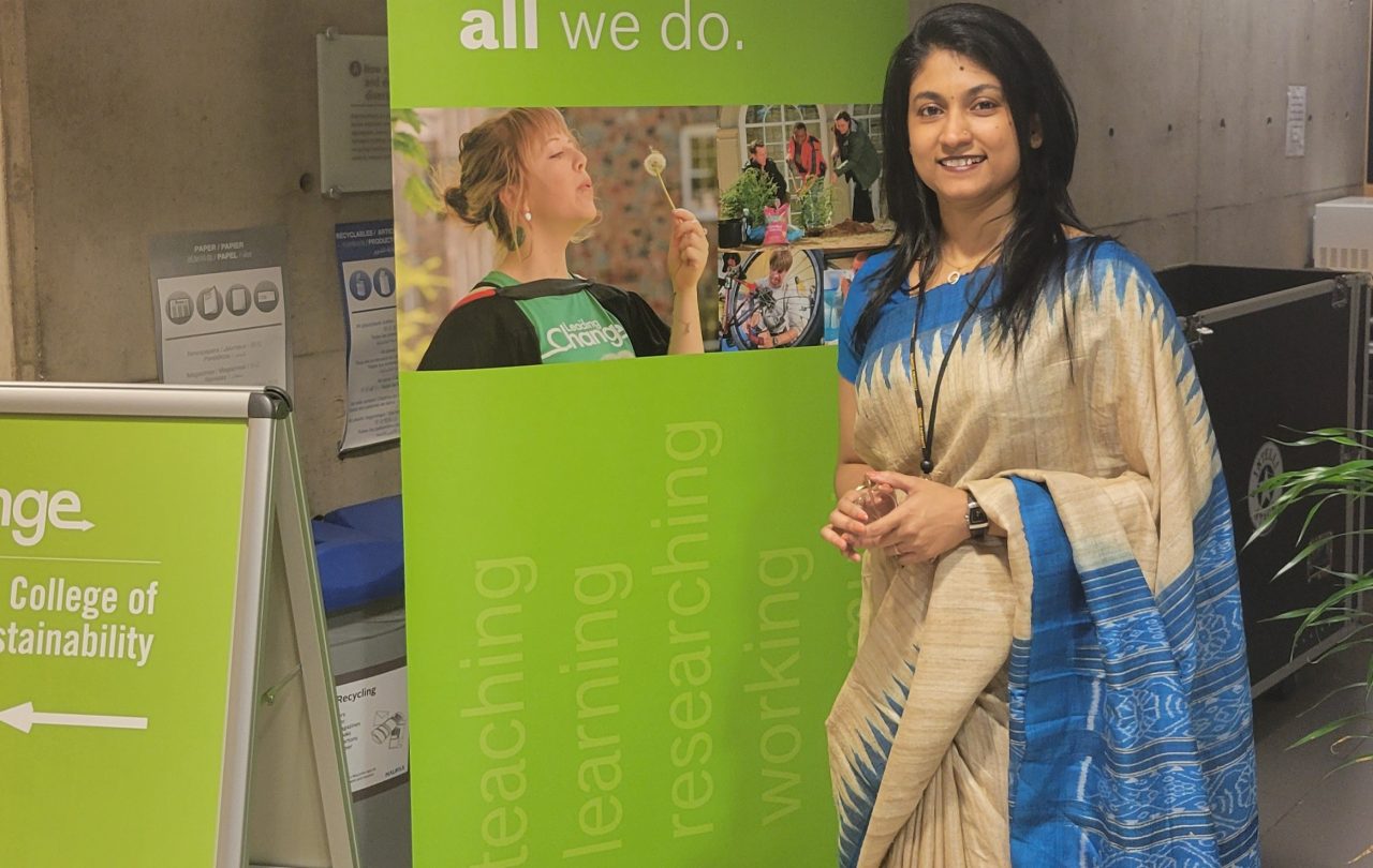 A female learner standing in front of a sign and smiling.