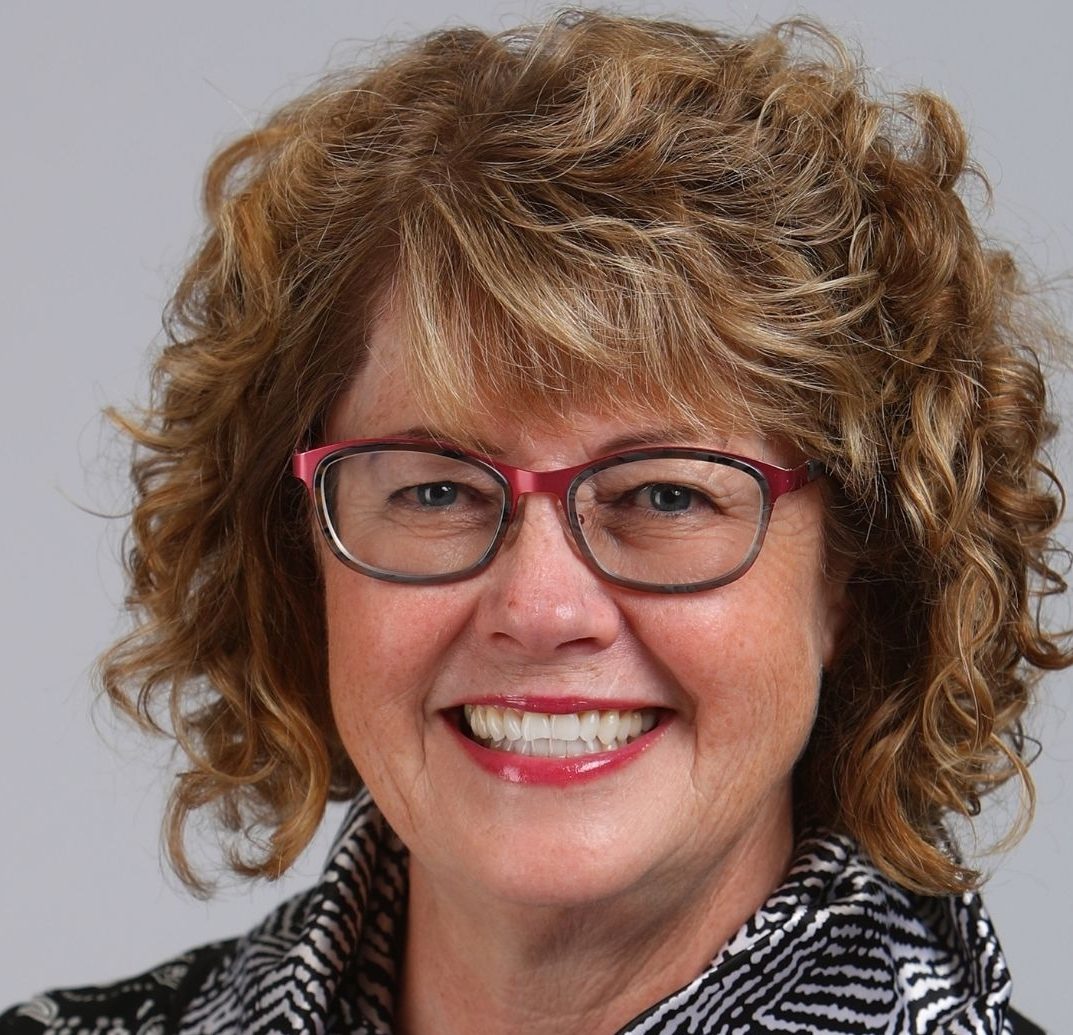 Woman with curly blonde hair wearing red glasses.