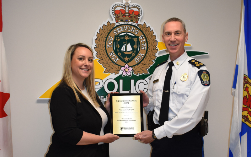 A female and a man in uniform are standing on either side of a plaque and holding it while smiling.