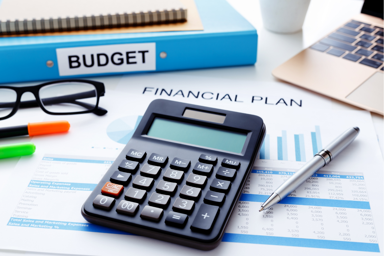 a calculator and pen lay atop a financial plan with laptop and other items.