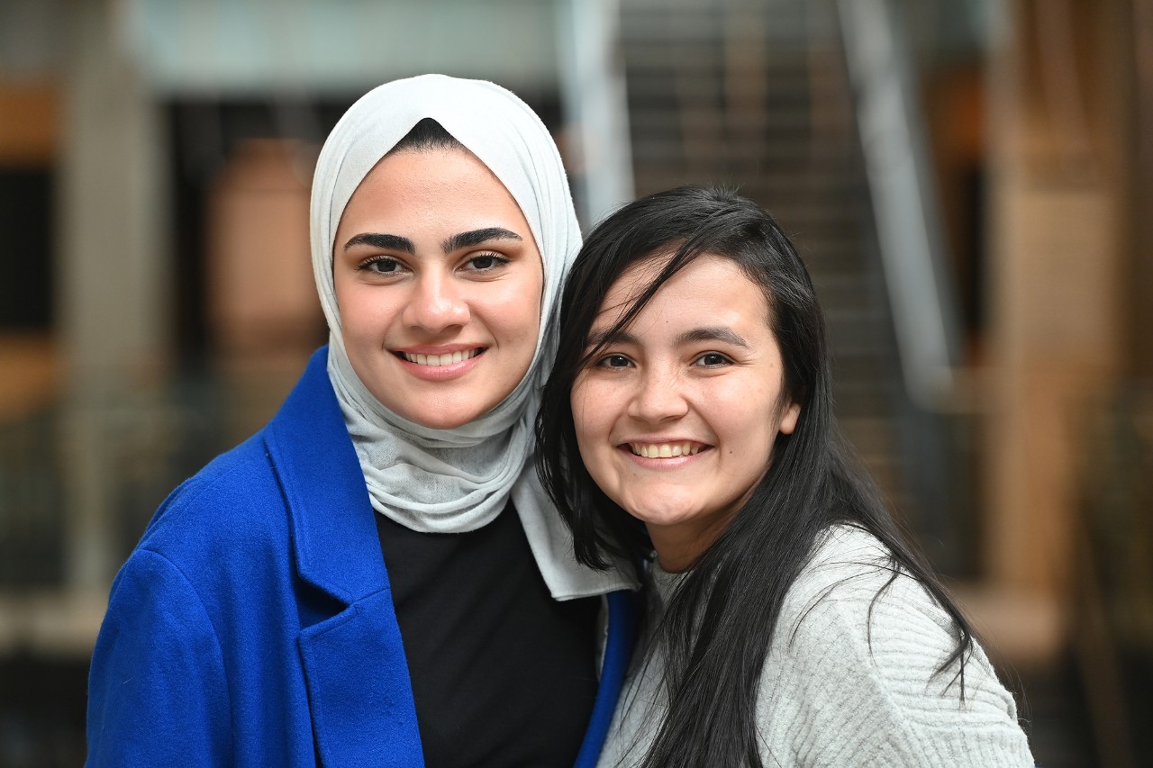 Two female students stand close together smiling.