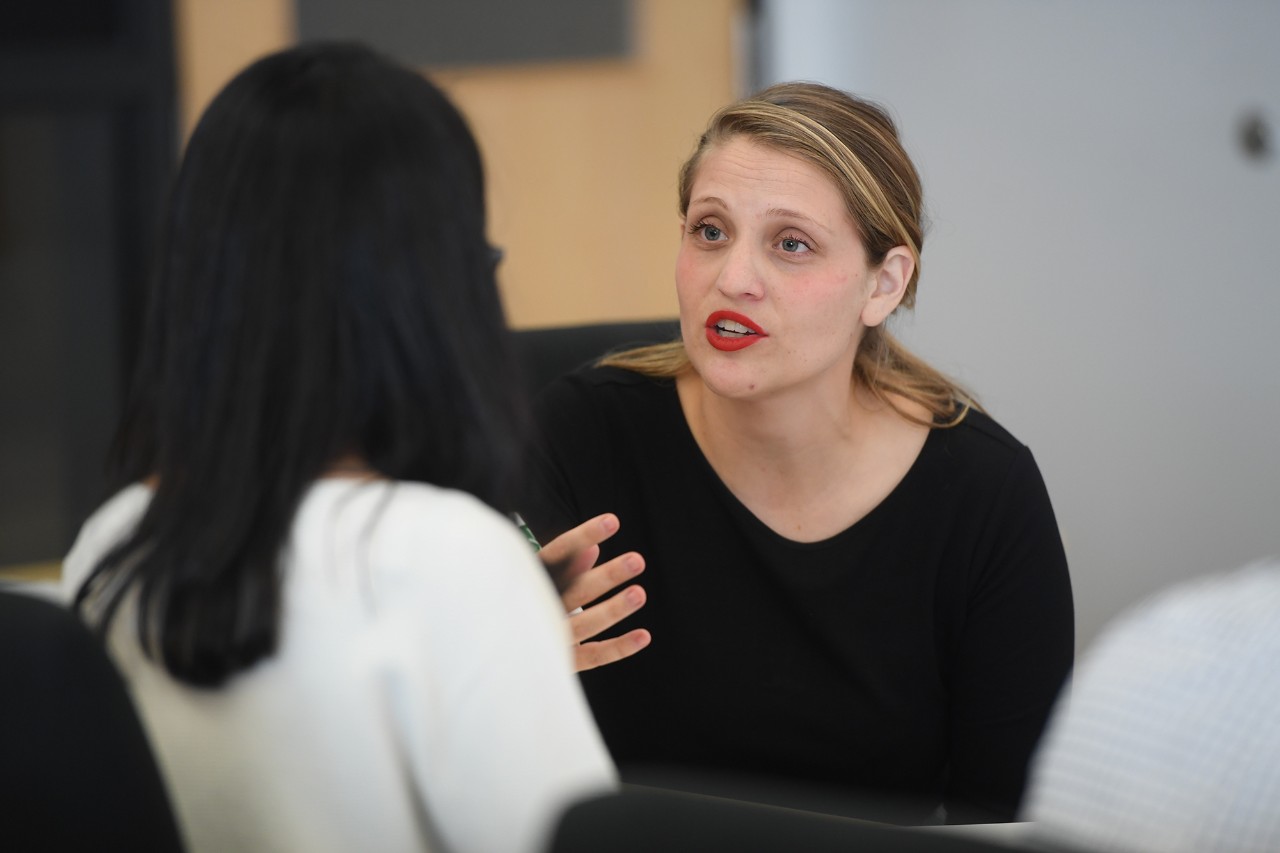 A blonde woman talks to a student with long black hair.