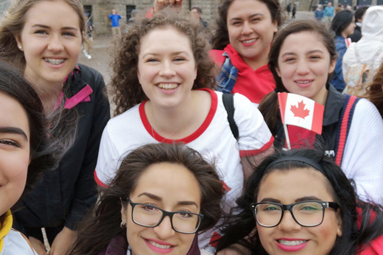 A small group of female students standing close to the camera waving Canada flags.