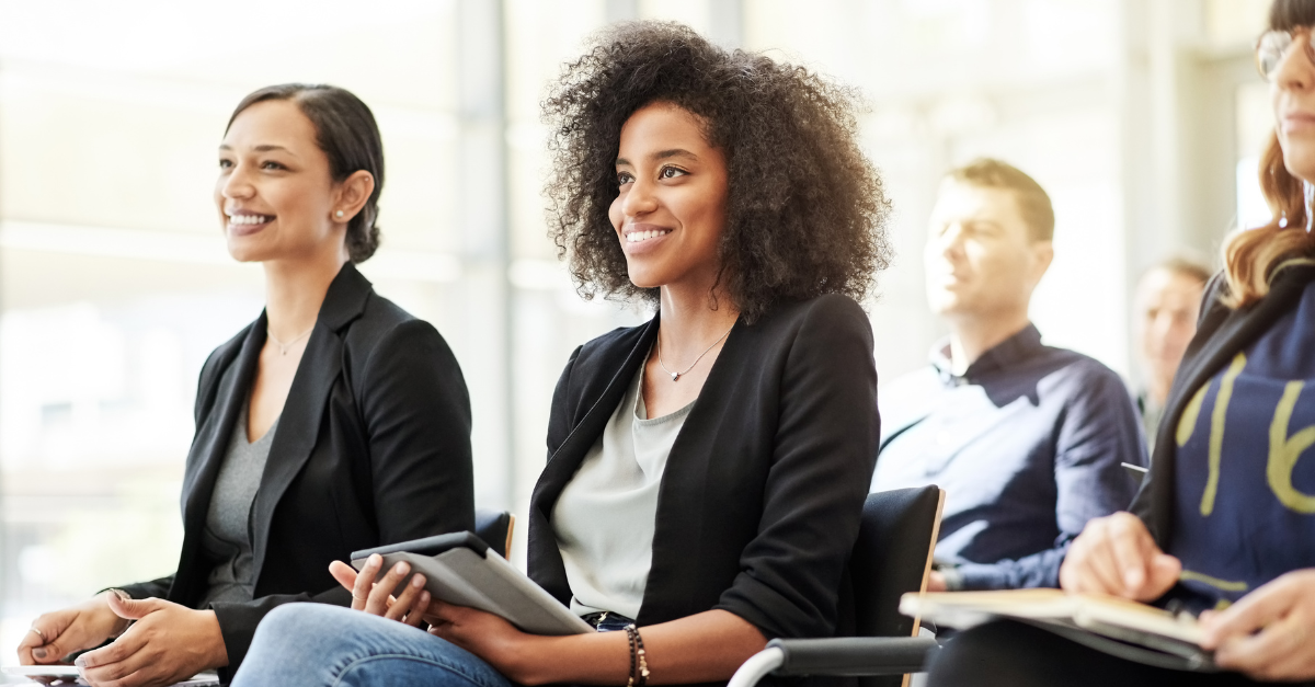 A close-up image of two women smiling giving the impression that they are energetically listening to a person speaking.