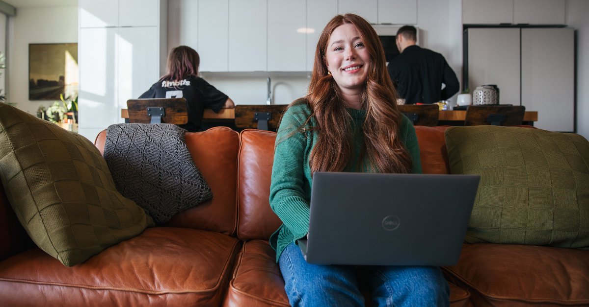 A woman on a laptop sitting on a couch with a young sitting behind her