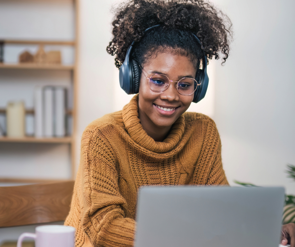 A femal student with headphones on working on a laptop