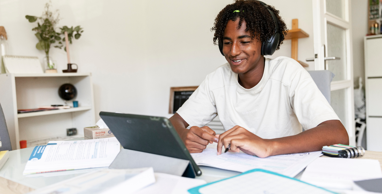 An student with headphones on learning on an ipad and working on school work.