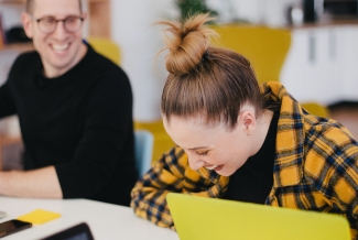 Two students working on laptops and laughing.