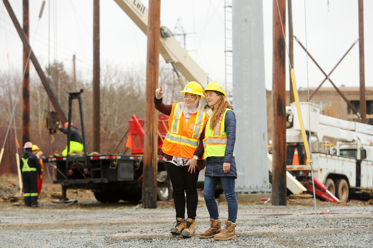 Two engineering students wearing yellow hard hats and safety vests on a construction site.