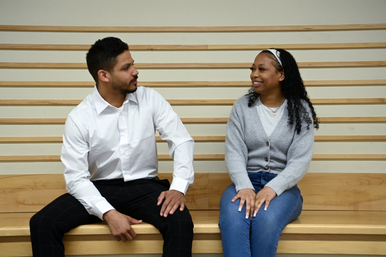 Two students sit on a wooden bench facing each other.