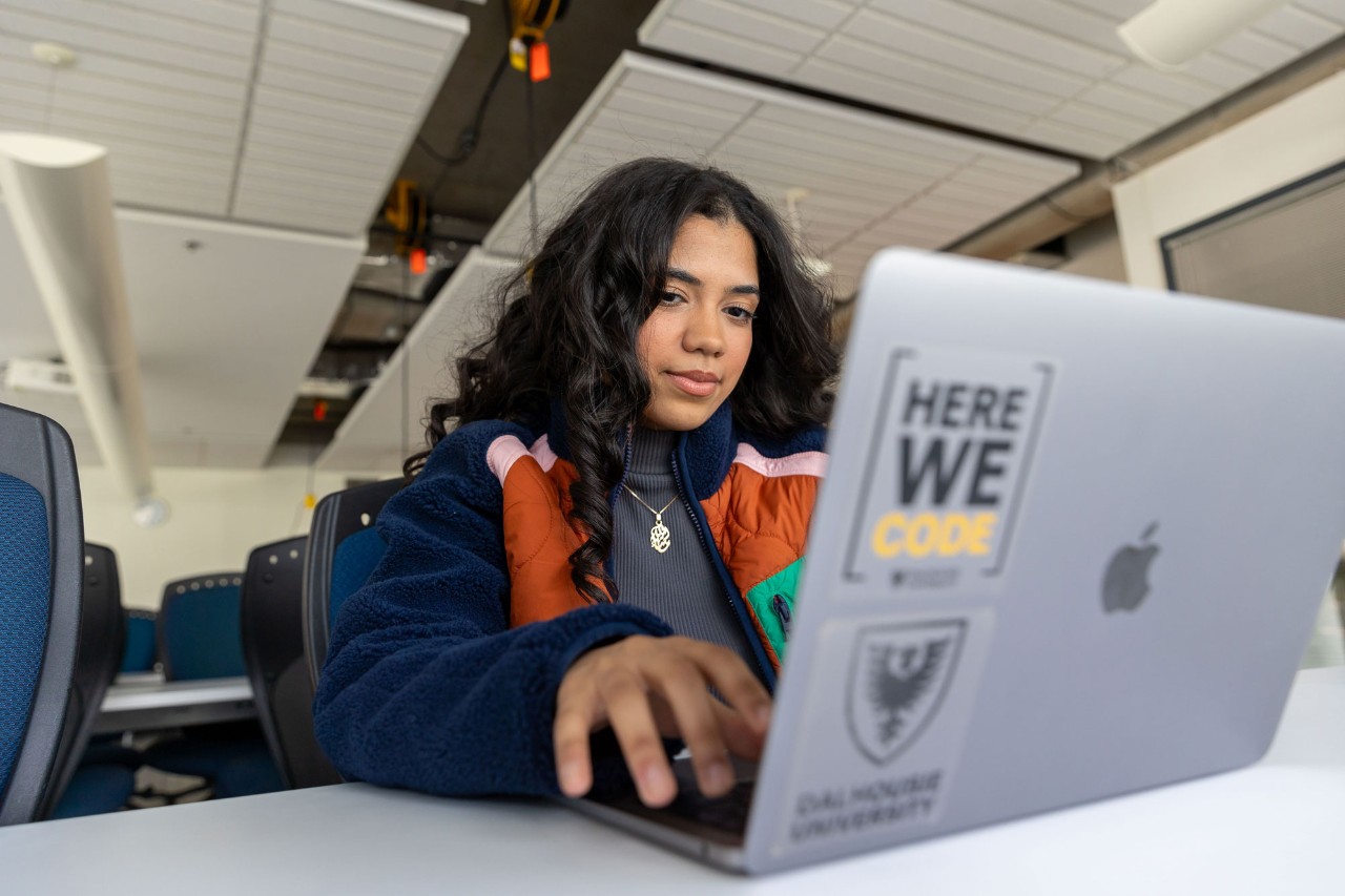 Student using laptop with a Here We Code sticker.