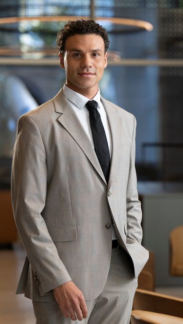 Daniel poses in a light-grey suit in an office.