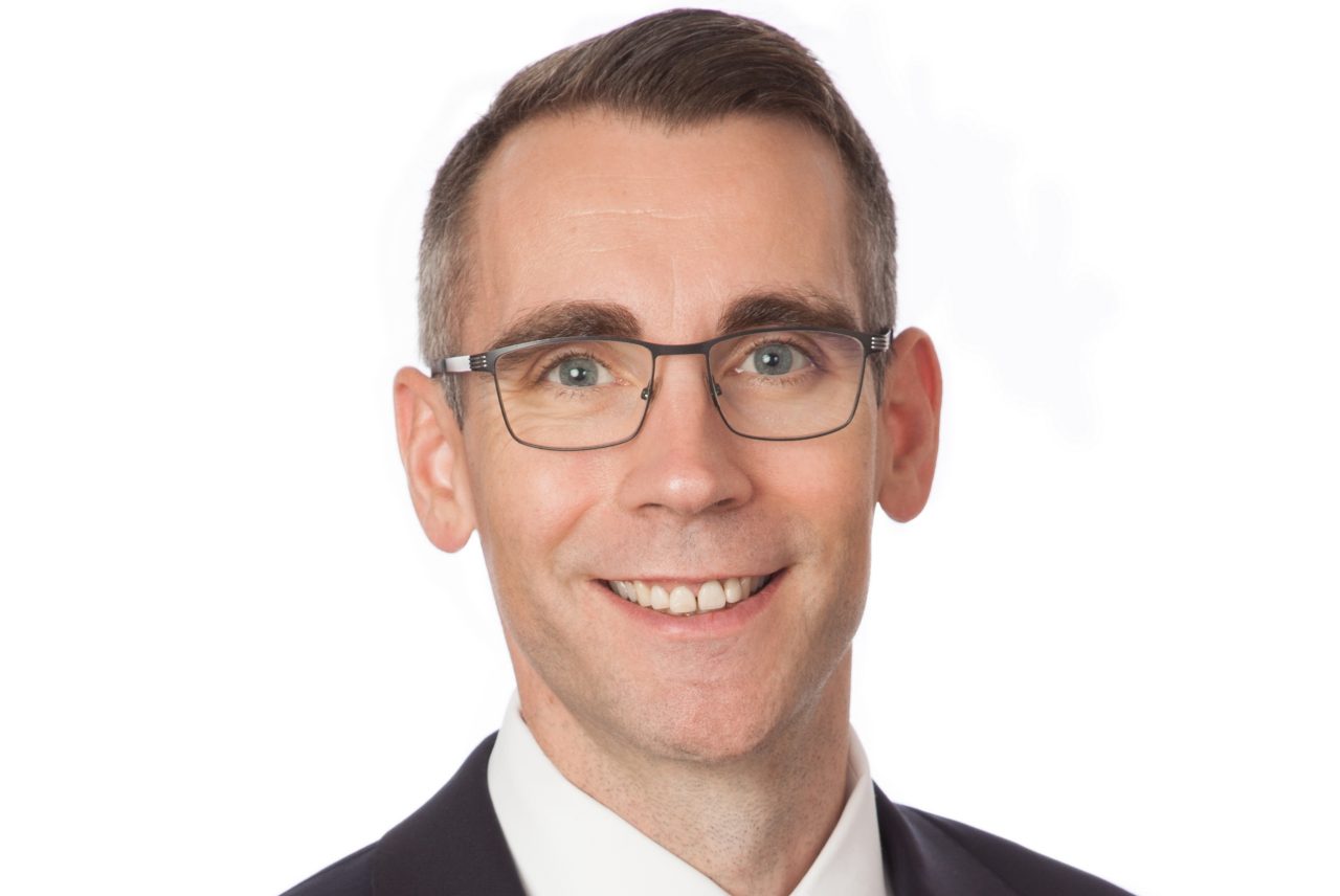 James McGuigan in a suit and red tie, smiling.