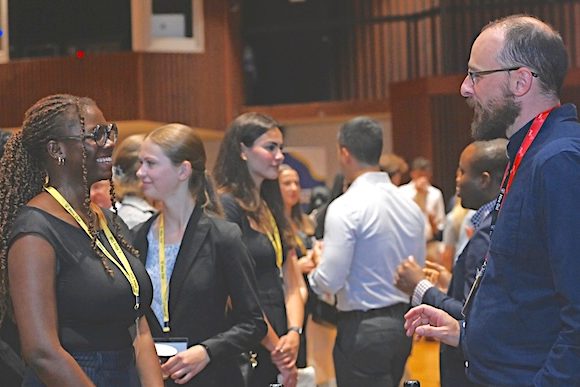 A student in conversation with an employer while guests mingle in the background. 