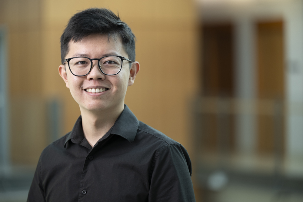 Chinese student Barry smiles at the camera, wearing a black collared shirt.  