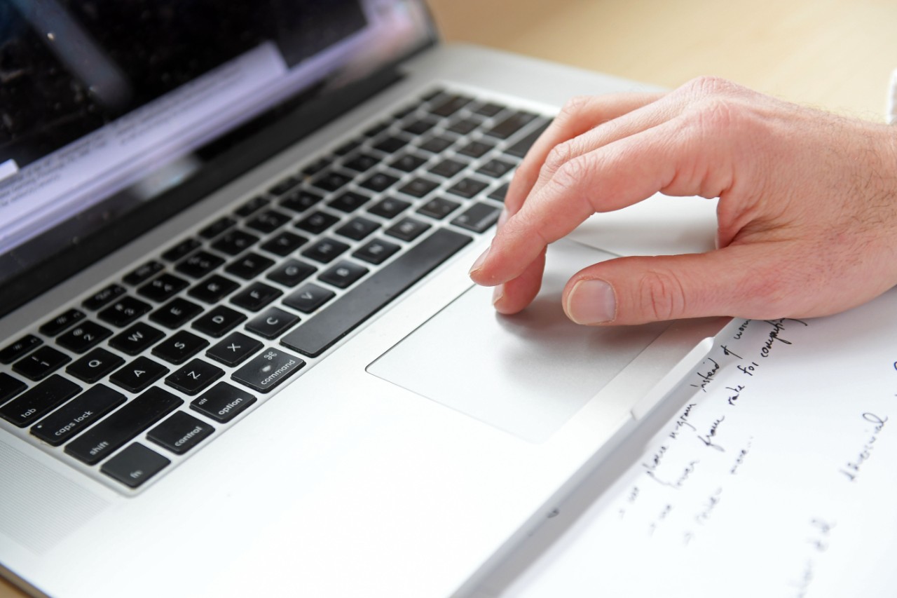 A close-up photo of a hand using the trackpad to scroll on a silver laptop.  