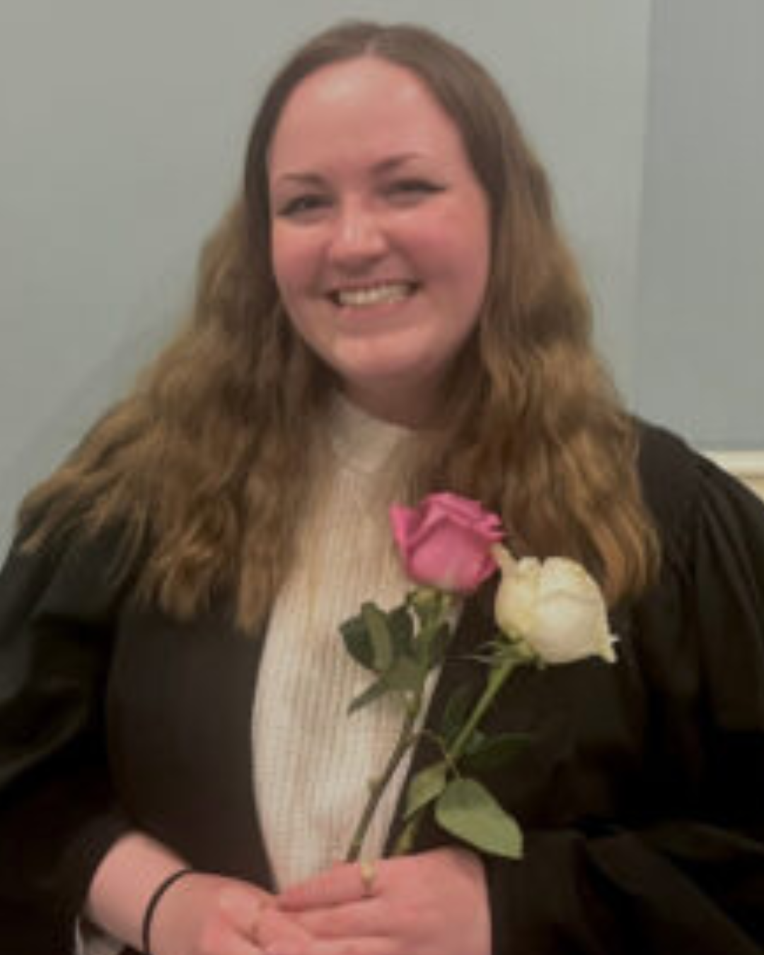 Erin Inglis smiling, wearing an academic gown and holding flowers