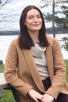 Law, Justice & Society grad Sydney Belford headshot sitting at a picnic table on a waterfront. 
