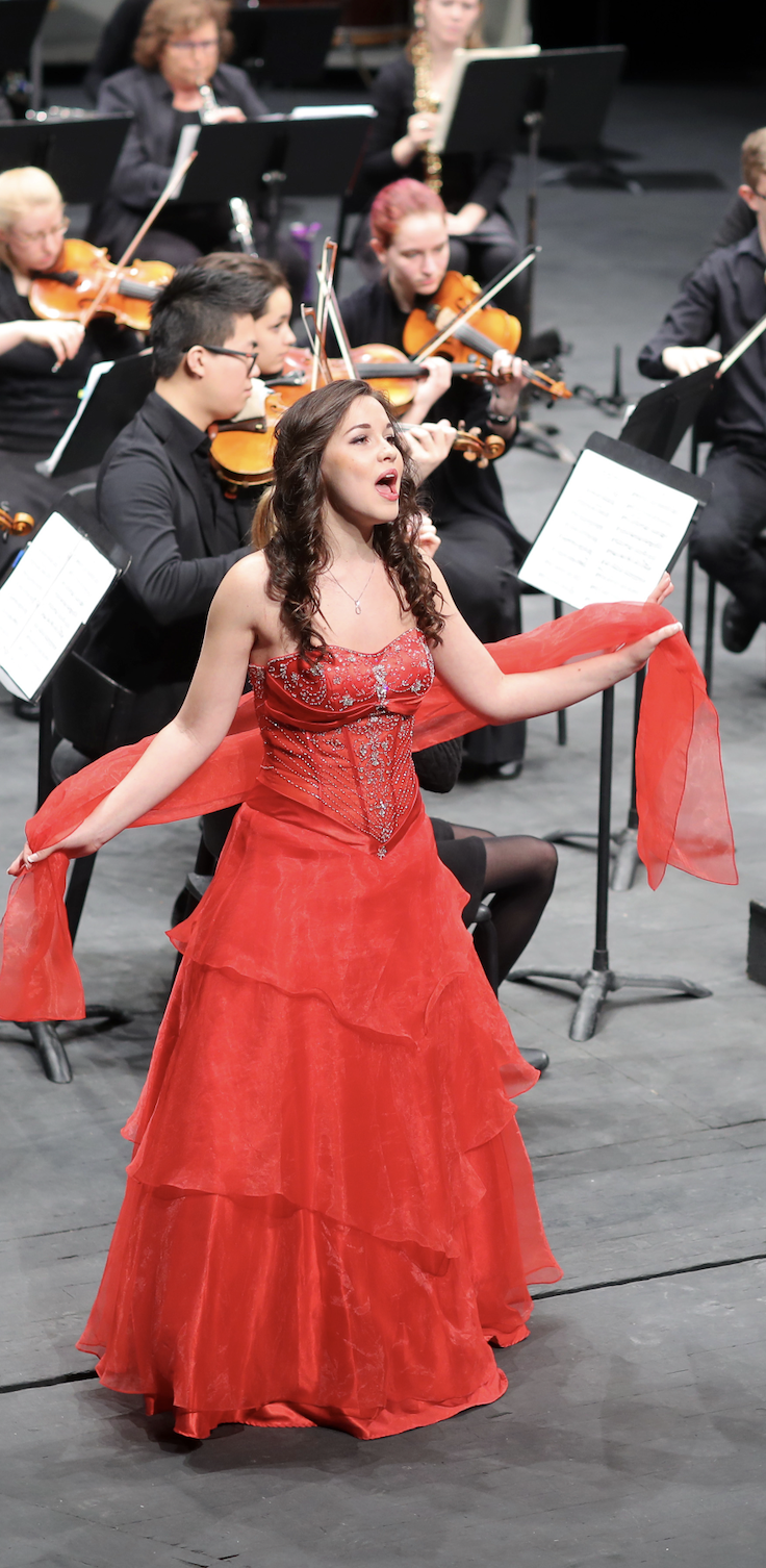Female Music student singing in red dress at concerto rehearsal