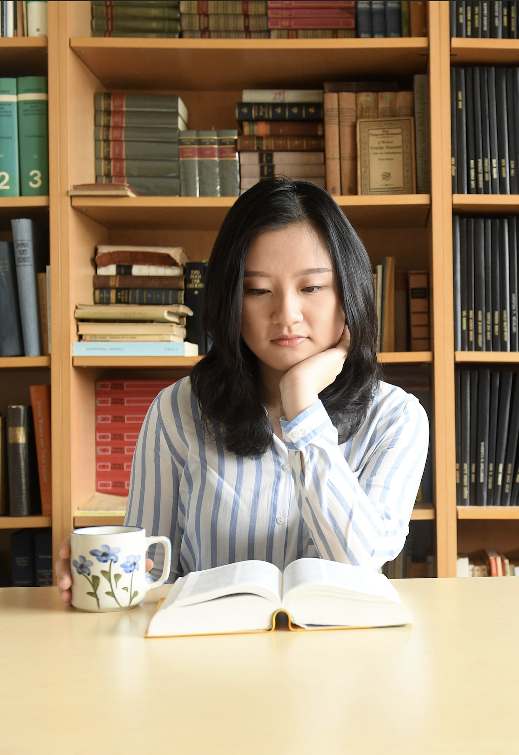 female student reading in a library with a cup of tea