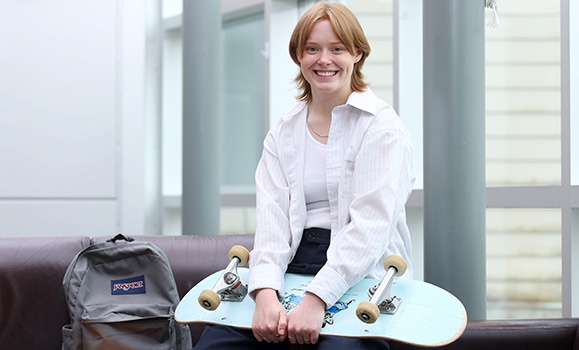 sosa grad sitting by a backpack and holding a skateboard